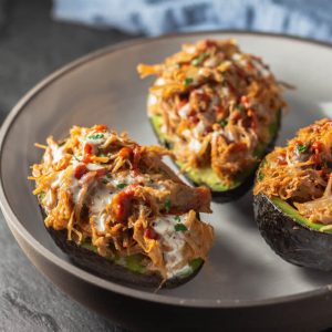 Stuffed avocados or avocado boats with pulled pork, cheese, and BBQ sauce in a bowl.