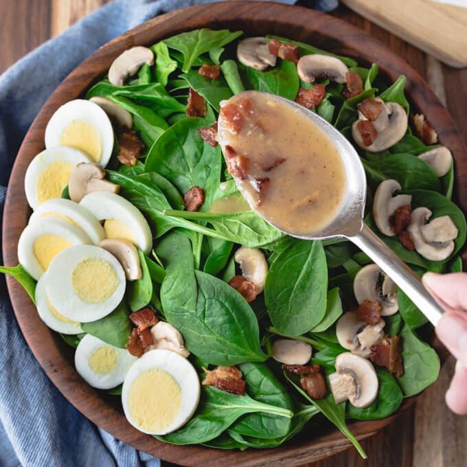 spinach salad with eggs and pecans and a spoon with bacon dressing