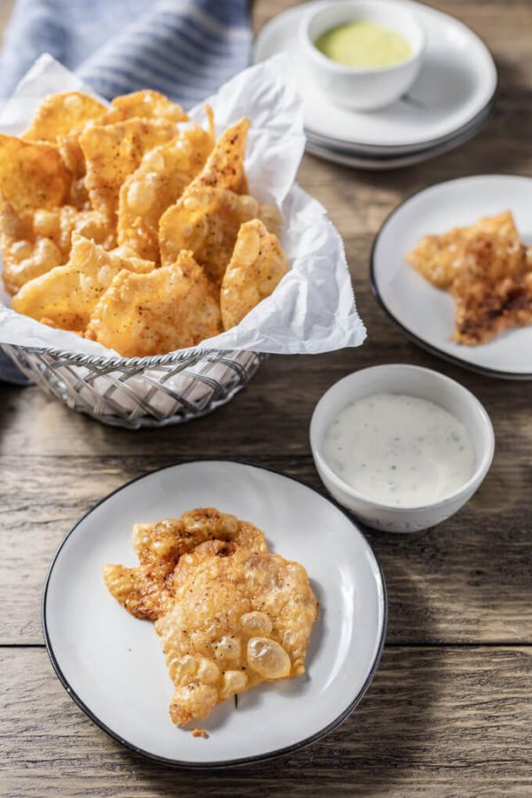 Crispy chicken skin cracklings or chicharrones in a paper lined basket and on a plate with dip.