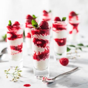 Keto raspberry sauce and cheesecake fluff layered in shot glasses like a parfait and topped with raspberries and mint.