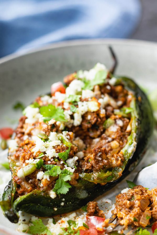 Poblano peppers stuffed with ground beef, cauliflower, cheese and cilantro on a plate with fork.