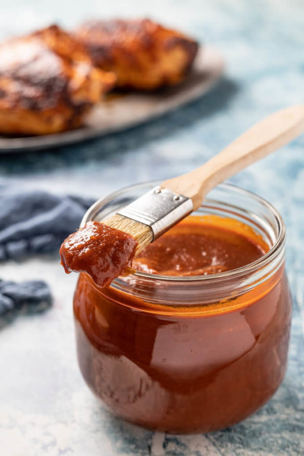 Homemade tomato based keto BBQ sauce in a jar with brush and BBQ chicken