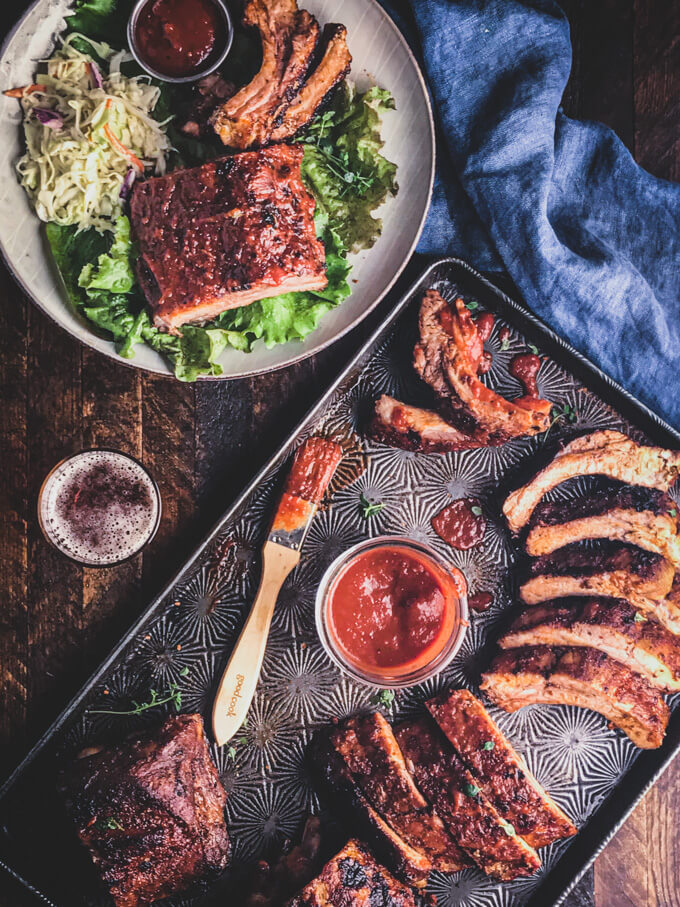 keto ribs on a sheet pan with BBQ sauce, and brush with bowl of salad ribs and keto coleslaw on the side.