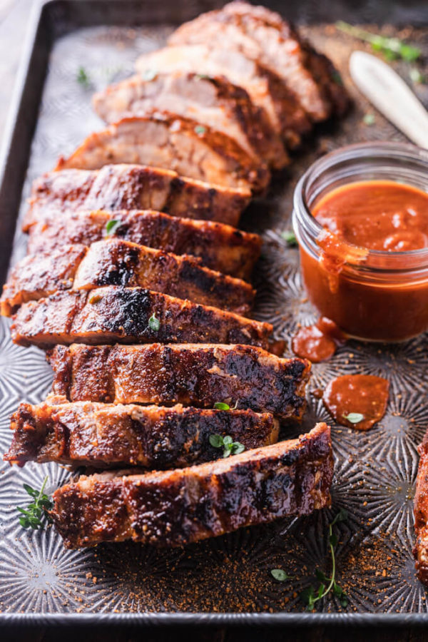 Sliced baby back rib rack slathered in bbq sauce with drips