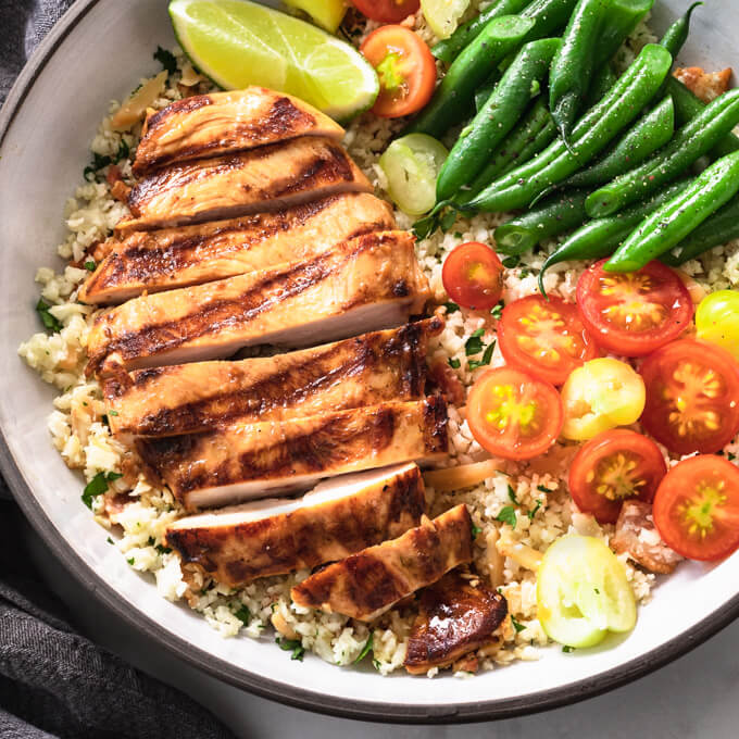 Sliced Key West chicken breast on cauliflower pilaf with vegetables in a bowl.