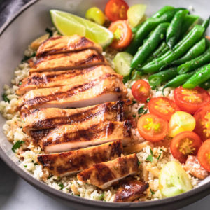 Sliced Key West chicken breast on cauliflower pilaf with vegetables in a bowl.