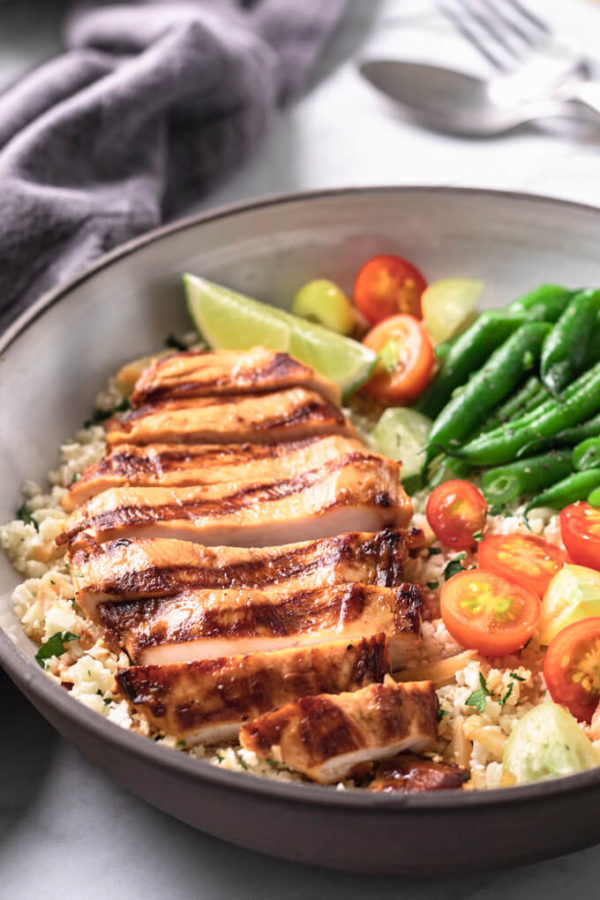 Sliced Key West chicken breast on cauliflower pilaf with vegetables in a bowl. 