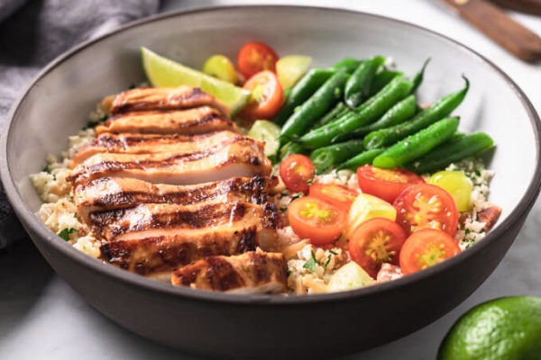 Grilled Key West chicken in a bowl with vegetables and a lime wedge.