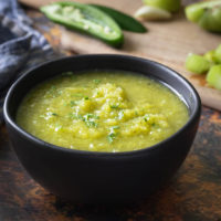 Green tomato salsa verde in a black bowl with jalapenos and cilantro