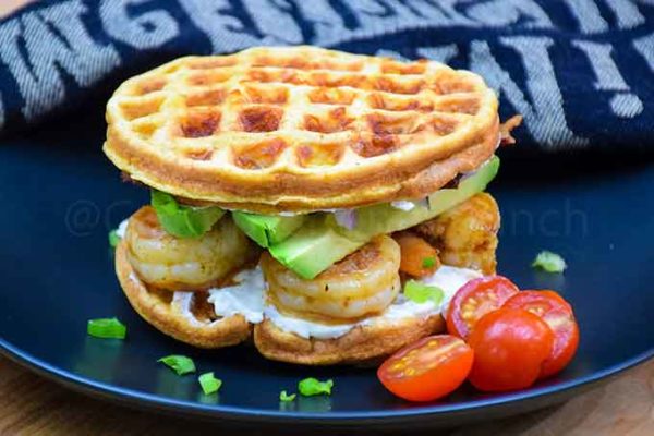 A whole chaffle sandwich on a plate with cherry tomato garnish