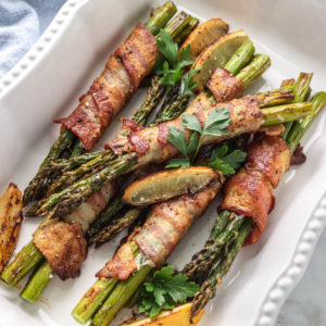 Bacon wrapped asparagus bundles with roasted lemons in a white serving dish