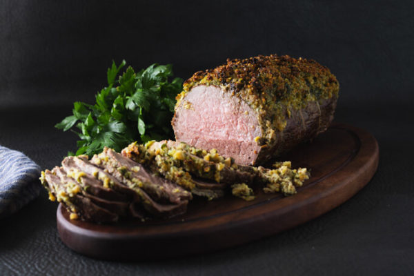 Sliced eye round roast beef with herb crust on a cutting board with parsley