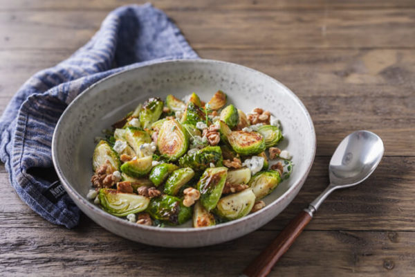 Quartered roasted Brussels sprouts in a bowl with walnuts, blue cheese and a sprig of thyme