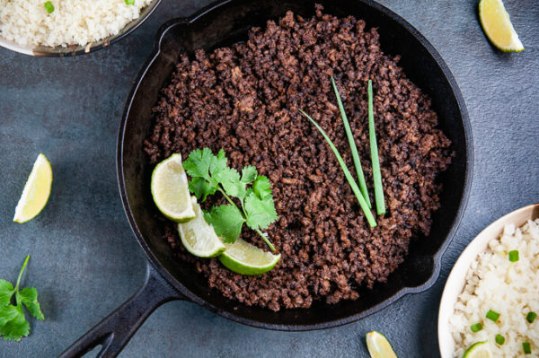 Ground beef with Korean flavors in a skillet with lime, cilantro and scallions.