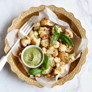 Roasted cauliflower florets in a bowl with pesto dipping sauce, basil and a fork