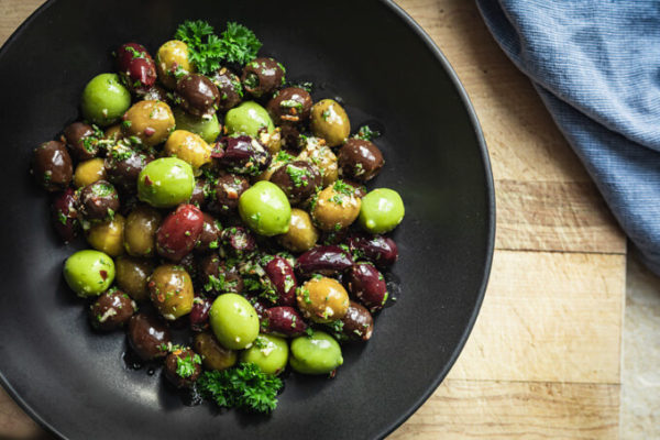 Green and black marinated olives with herbs, spices, garlic, oil and vinegar with parsley in a black bowl