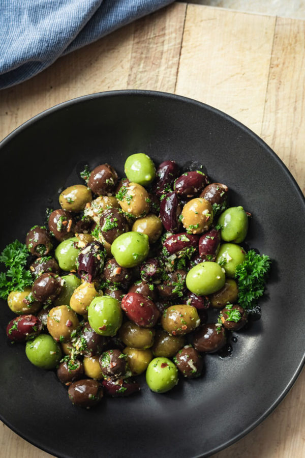 Green and black marinated olives with herbs, spices, garlic, oil and vinegar with parsley in a black bowl