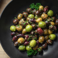 Green and black marinated olives with herbs, spices, garlic, oil and vinegar with parsley in a black bowl