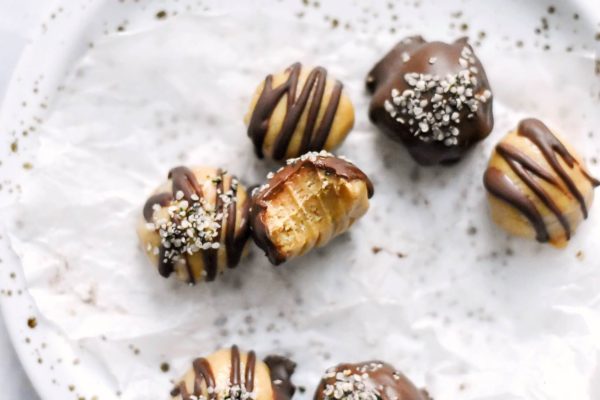 Peanut butter truffles with chocolate on a plate, a bite out of one truffle shows the creamy texture