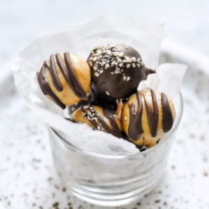 Pretty chocolate covered vegan keto peanut butter truffles in a parchment lined glass