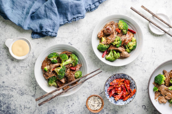 Keto beef and broccoli with dried red peppers in bowls with chopsticks and Chinese mustard.