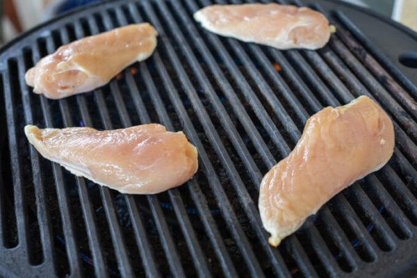 How to make grilled shredded chicken: 4 raw chicken breast halves cooking on a grill.