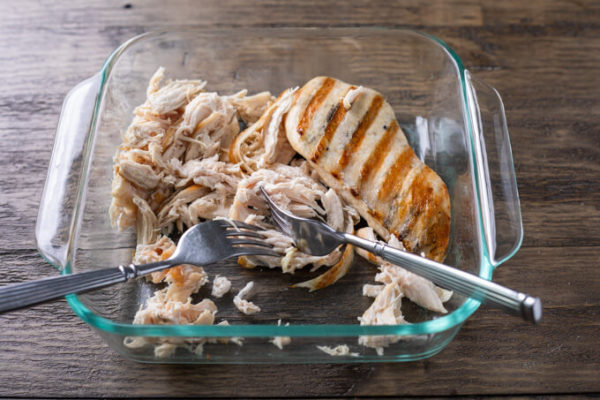 How to shred chicken: 2 grilled chicken breasts, one shredded and own whole) in an 8x8 glass baking dish with two forks.