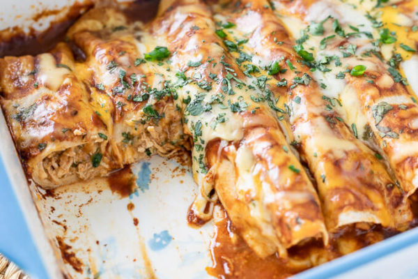 Cooked BBQ chicken enchiladas topped with melty cheese and cilantro in a baking dish.