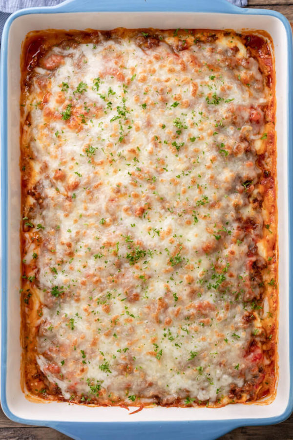 Top down image of baked keto eggplant lasagna with meat sauce in a blue and white casserole dish topped with chopped parsley. 