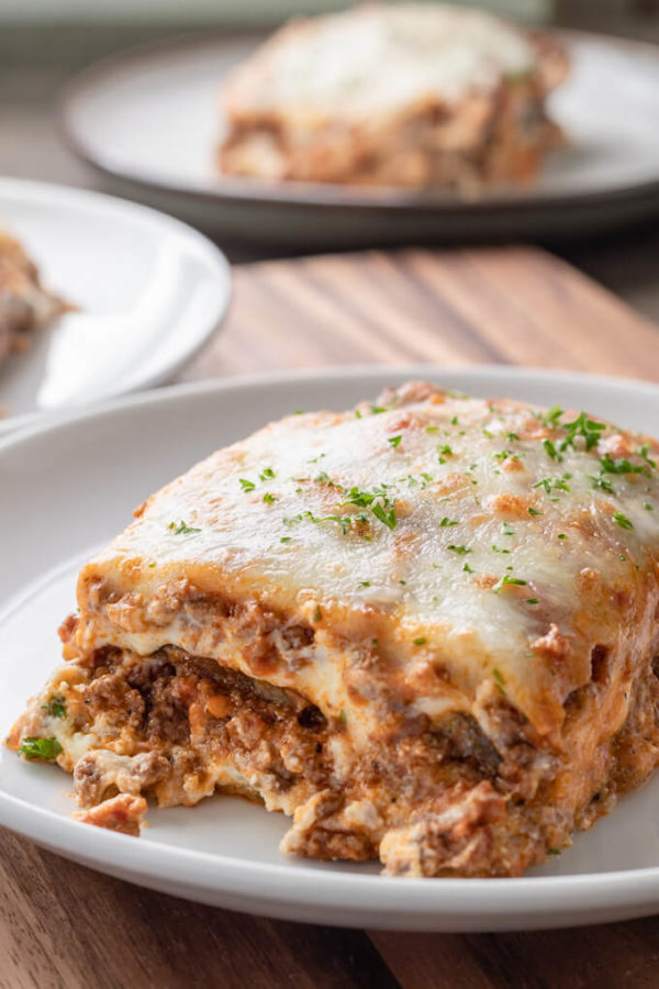 Slice of eggplant lasagna with meat sauce topped with chopped parsley on a white plate.