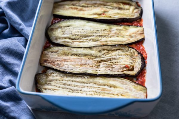 tomato sauce topped with sliced eggplant placed side-by-side in a lasagna pan
