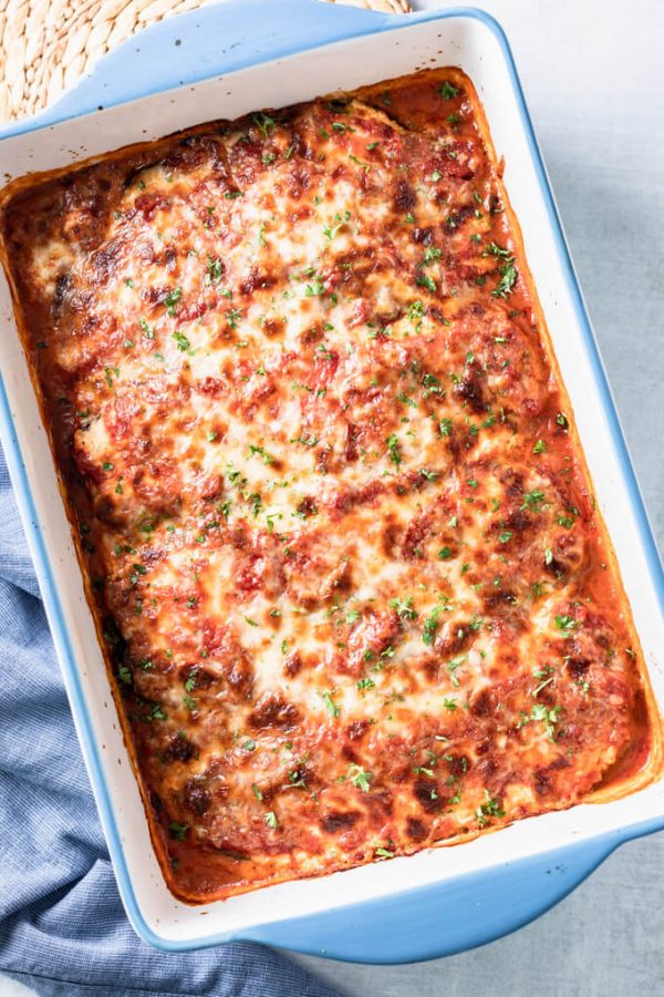 baked vegetarian keto lasagna in blue rimmed lasagna pan topped with parsley and blue napkin to the side.