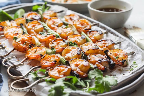 Keto teriyaki shrimp skewers on platter with cilantro; bowl of sauce behind.