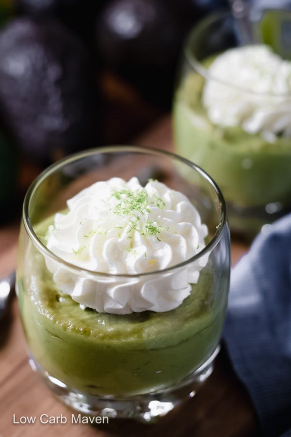 Keto avocado pudding in a glass topped with whipped cream and grated lime zest with napkin to side