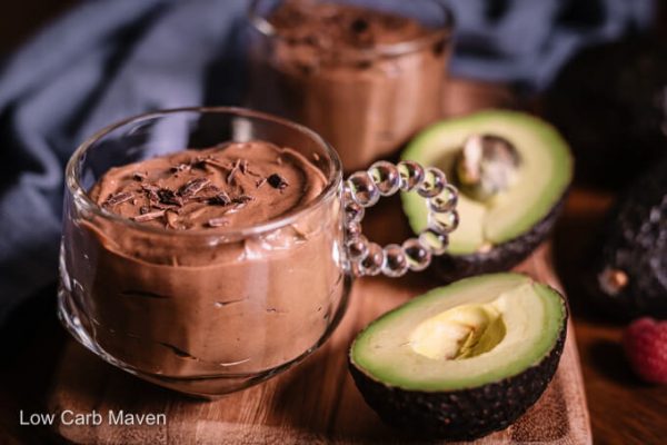 Creamy keto chocolate avocado pudding in cup with halved avocado and napkin behind.