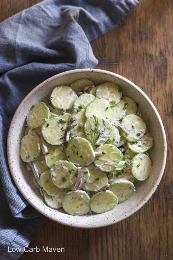 Creamy cucumber salad or German cucumber salad in white bowl on table with napkin beside