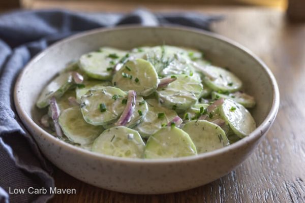 Keto cucumber salad with creamy dressing purple onion and fresh chopped herbs in white bowl