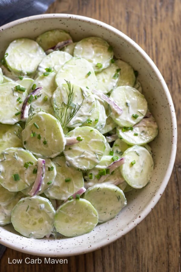Keto cucumber salad in white bowl: sliced cucumbers with creamy dressing, purple onions, snipped chives and dill.